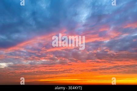 Stunning sunset sky filled with textured clouds glowing in shades of orange, pink, and blue, creating a dramatic and colorful natural background. Stock Photo
