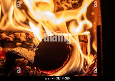 Bright yellow and orange flames wrap around a burning wooden log inside a cozy fireplace or wood-burning stove. Stock Photo