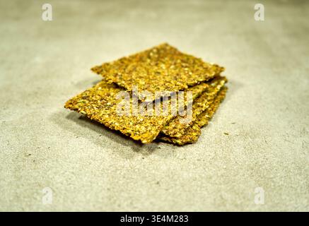 A stack of four rectangular seed crackers or crispbreads arranged on a light gray textured surface, possibly concrete or stone. The crackers have a Stock Photo