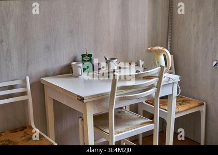 A small dining area featuring a white wooden table and three matching chairs with cushioned seats positioned against light wood-paneled walls. On the Stock Photo
