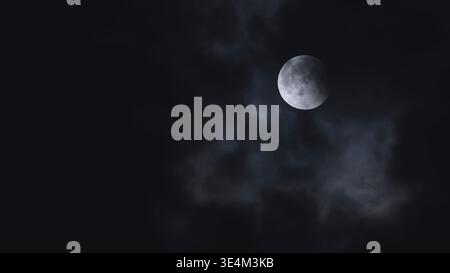 Lunar eclipse moon phase glowing behind mysterious clouds in a dark night sky Stock Photo