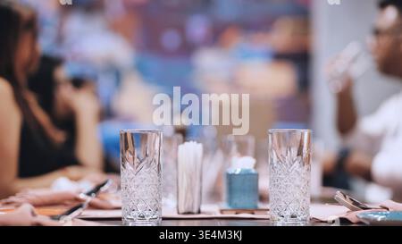 Elegant dinner table setting with crystal glasses in focus and people blurred in the background Stock Photo
