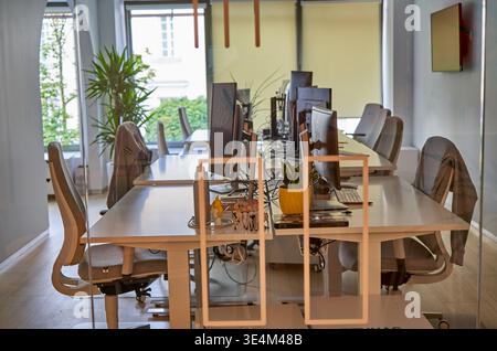 A modern office interior featuring rows of white desks equipped with computer monitors, keyboards, and office supplies. Several ergonomic office Stock Photo