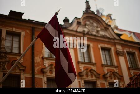 A low-angle, street photography shot featuring the national flag of Latvia (carmine red with a white horizontal stripe) prominently displayed on a woo Stock Photo