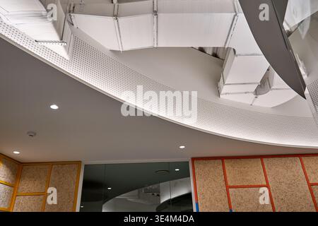 Low angle view of a contemporary office interior ceiling featuring exposed white HVAC ductwork and ventilation systems mounted on curved white Stock Photo