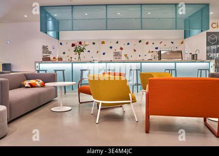 A modern, brightly lit interior space featuring a contemporary office lounge or coworking cafe area. The foreground shows comfortable seating Stock Photo