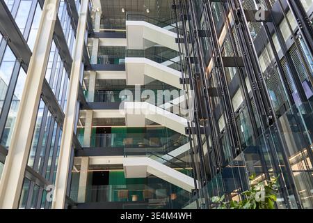 Modern multi-level interior atrium of a contemporary office building featuring a prominent white floating staircase with glass railings. The Stock Photo