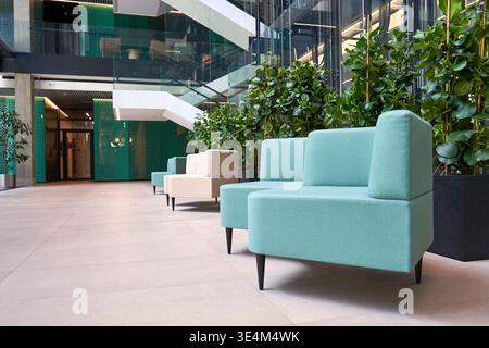 A modern corporate lobby or atrium interior featuring contemporary modular seating upholstered in turquoise fabric with black tapered legs, arranged Stock Photo