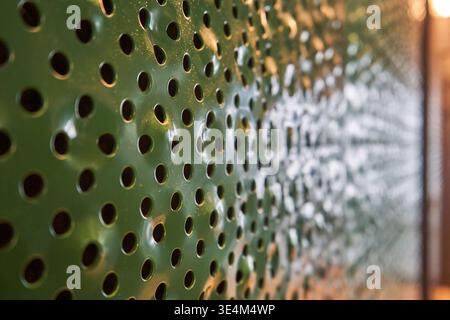 A close-up perspective shot of a green painted perforated metal panel with circular holes arranged in a regular grid pattern. The left side of the Stock Photo