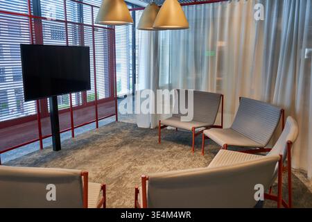 Modern interior meeting space or lounge area featuring four grey upholstered chairs with red metal frames arranged in a semi-circle facing a large Stock Photo