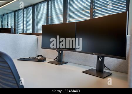 Modern office workspace featuring two Dell computer monitors positioned side by side on a white desk. The dual-monitor setup includes ergonomic Stock Photo