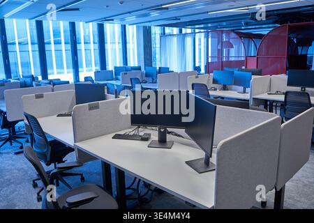 A modern, empty open-plan office interior featuring multiple white workstations with light gray fabric privacy dividers. Each desk is equipped with Stock Photo