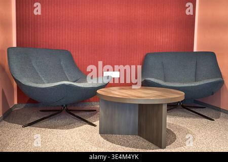 A modern interior lounge area featuring two contemporary gray upholstered armchairs with curved silhouettes and black swivel star bases positioned on Stock Photo
