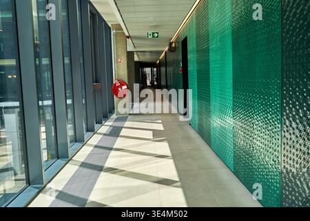 A modern, empty corridor in a contemporary office building or public facility, featuring a vibrant green textured wall on the right side with a Stock Photo