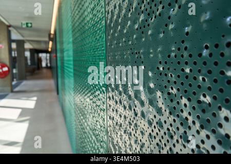 A modern interior corridor featuring a perforated green metal screen wall with varying hole sizes creating an abstract geometric pattern. The Stock Photo