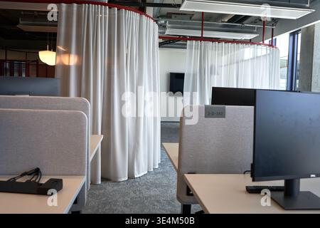 A modern office interior featuring individual workstations with light gray fabric partitions and white desks equipped with black computer monitors Stock Photo