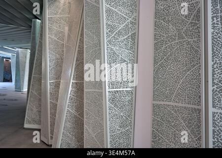 A contemporary interior architectural space featuring a series of tall, vertical perforated metal panels arranged in a rhythmic sequence receding Stock Photo