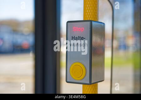 Yellow stop request button mounted on a pole inside a public transportation vehicle with the word stop illuminated in red and blurred outdoor backgrou Stock Photo