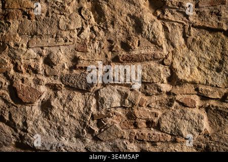 Rough ancient stone and rock wall showing weathered texture and uneven surface, forming a rugged historical background or natural pattern Stock Photo