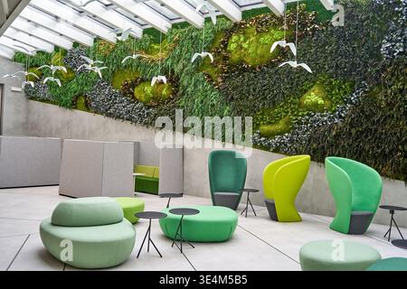 A modern office interior featuring a large biophilic living wall covered in various mosses, ferns, and plants spanning the back wall beneath a glass Stock Photo