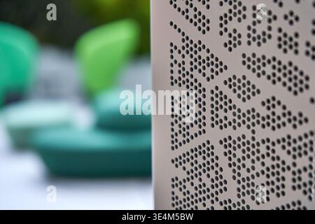Close-up of a modern perforated metal panel featuring a geometric pattern of circular holes, positioned in sharp focus on the right side of the Stock Photo