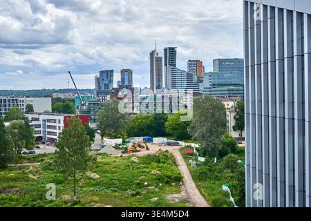 Aerial view of urban development showing a construction site in the foreground with dirt paths, an excavator, construction materials, and patches of Stock Photo
