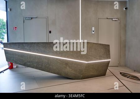 A modern, minimalist reception area featuring a large angular reception desk made of stone or concrete composite material with integrated LED strip Stock Photo