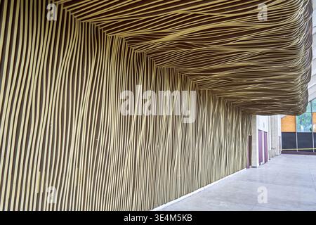 A covered outdoor walkway or corridor featuring an architectural installation with distinctive wavy striped patterns covering the wall and ceiling Stock Photo