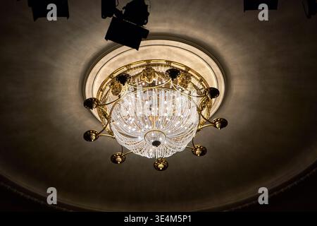 A low-angle view of an ornate crystal chandelier suspended from a domed ceiling. The chandelier features elaborate gold or brass metalwork with Stock Photo