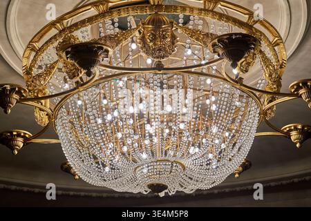 Low angle view of an ornate, classical crystal chandelier suspended from an elaborate ceiling. The luxurious lighting fixture features intricate Stock Photo
