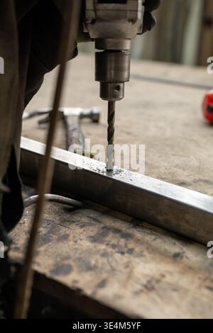 Close-Up of a Skilled Male Craftsman Using a Drill to Create Precision Holes in Metalwork on a Wooden Surface Stock Photo
