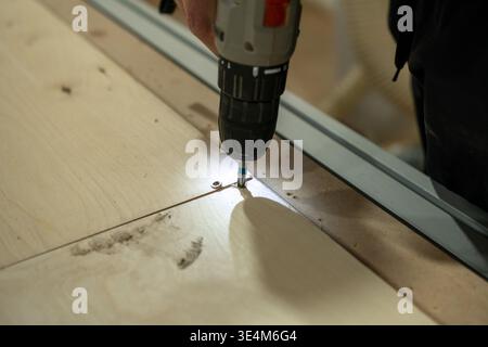 Focused Male Carpenter Using Power Drill to Secure Wooden Plank on a Workbench in a Workshop Environment Stock Photo