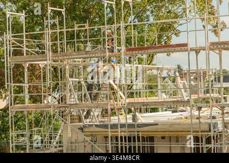 Berlin, Germany - September 01, 2025: Construction workers are collaborating on scaffolding at a building site surrounded by trees. Stock Photo
