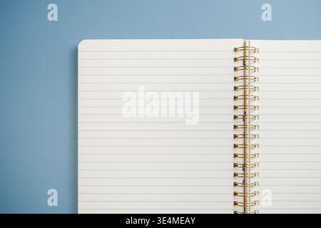 Blank spiral notebook lies open on a blue background. Open pages are lined and ready for writing or drawing. Top view Stock Photo