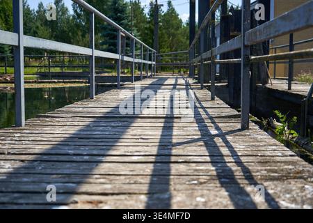 A weathered wooden pier or walkway extends over calm water, captured from a low angle perspective that emphasizes the rough texture of aged wooden Stock Photo