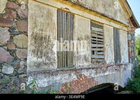 Weathered exterior wall of an abandoned old building featuring mixed construction materials including irregular stone masonry, red bricks, and Stock Photo