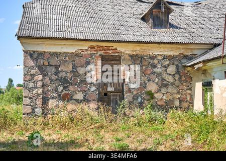 An abandoned old stone building with a weathered corrugated metal roof, featuring a rustic facade constructed from irregular fieldstones in various Stock Photo