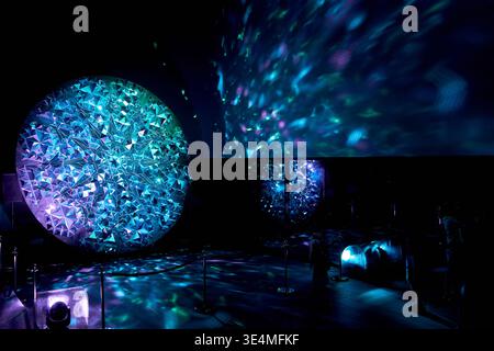 An immersive light art installation at a festival featuring a large circular structure covered in geometric triangular mirror pieces that reflect Stock Photo