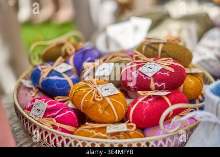 A close-up photograph of a white wicker basket filled with colorful handmade felted soaps displayed at what appears to be an outdoor craft market. Stock Photo