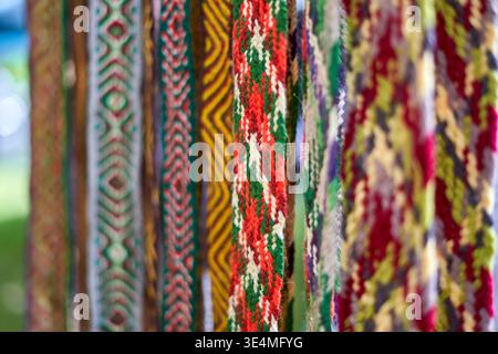 Close-up view of multiple colorful traditional woven textile sashes or ribbons hanging vertically side by side. The textiles feature intricate Stock Photo