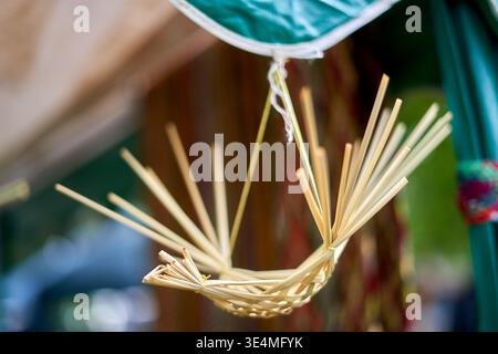 A close-up photograph of a miniature handcrafted woven straw object resembling a cradle or decorative basket, suspended from a green fabric canopy by Stock Photo