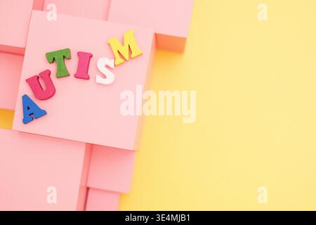 Word Autism made of colorful letters and pink cubes on yellow background. Top view Stock Photo