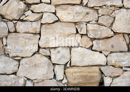 Texture of a traditional dry stone wall built from irregular beige and grey limestone blocks. Natural rustic background of old rock masonry. Stock Photo