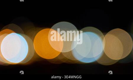 Abstract night background with colorful blurry bokeh lights in orange, blue, and white tones. Soft out of focus circular shapes on dark background. Stock Photo