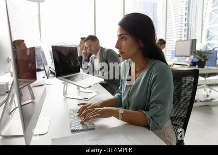 Focused Latina woman typing on desktop pc at shared office Stock Photo