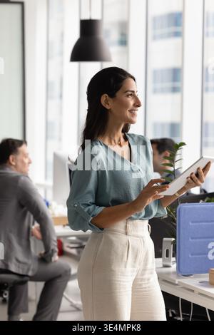 Smiling Hispanic female employee with digital tablet planning work Stock Photo