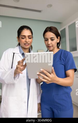 Two young diverse women medical workers using tablet at workplace Stock Photo