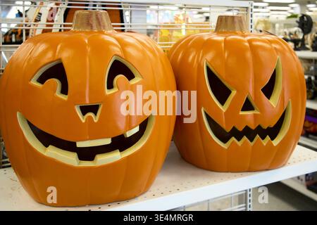 Two orange Jack-o'-lantern decorations on a store shelf. One with a happy smiling face and the other with a scary expression for Halloween decor. Stock Photo