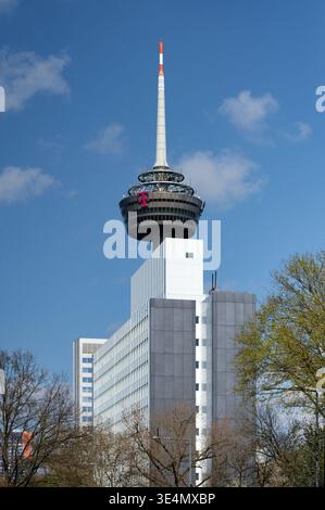 Cologne, Germany March 27 2026: Cologne landmark: The Colonius TV tower towers above the modern Telekom building, framed by spring trees against a blu Stock Photo