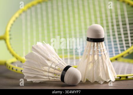 Badminton racket and shuttlecocks on wooden table against blurred green background, closeup Stock Photo